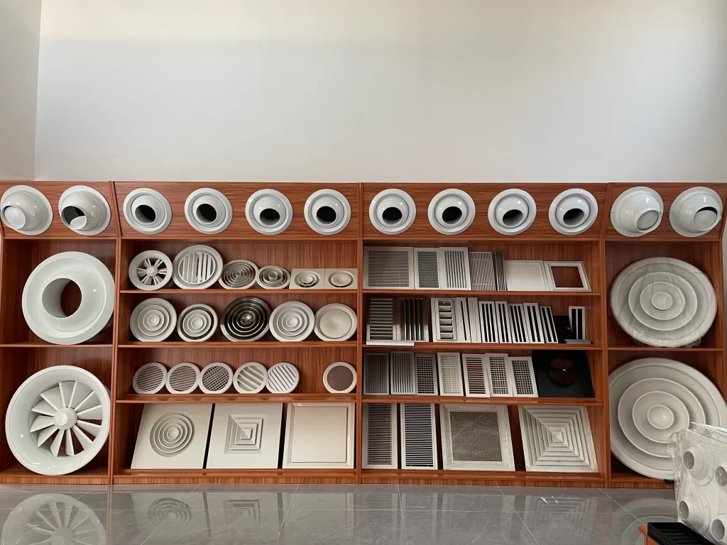A wooden display rack exhibits various ceiling diffuser samples, covering circular, square, linear shapes, and different sizes, offering a visual reference for selection.