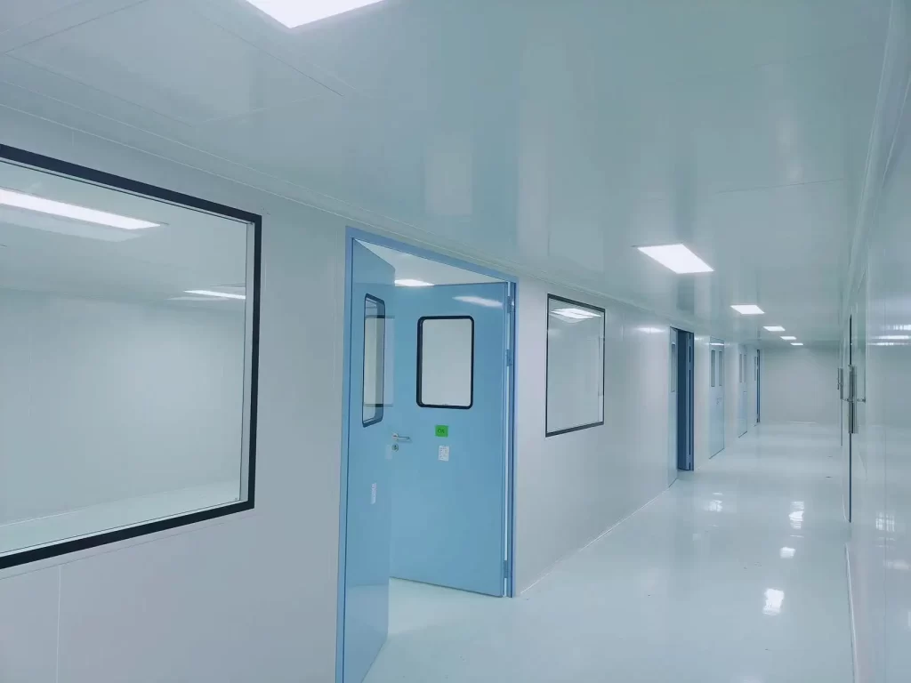 Airtight door in a cleanroom corridor (light blue finish, transparent vision panels), demonstrating particle control and pressure stability in positive-pressure environments (e.g., pharmaceutical, semiconductor facilities).