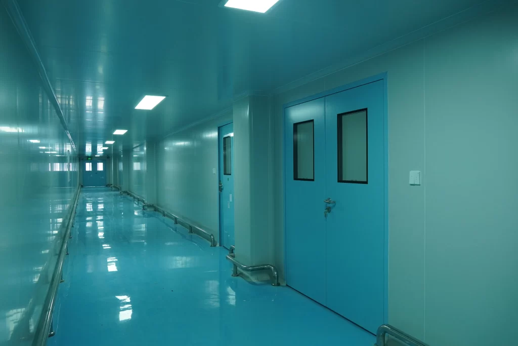  Displays a cleanroom corridor environment. Blue cleanroom doors are installed on both sides. The floor, walls, and ceiling feature clean - finish designs, presenting the overall cleanroom space and the application scenario of cleanroom doors.