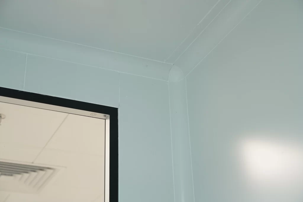 Provides a close - up of a cleanroom wall, ceiling corner, and cleanroom door frame finishing. Highlights details like gap sealing and flatness treatment, relevant to the installation foundation for cleanroom door sealing performance.