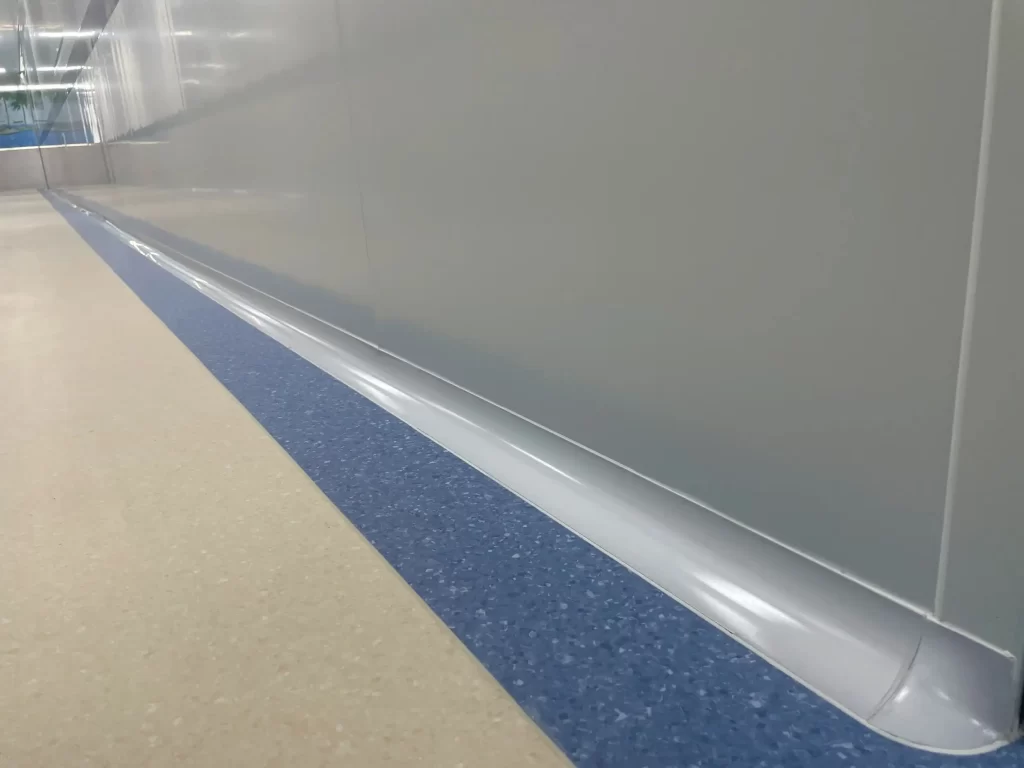 Cleanroom floor edge detail featuring a corrosion-resistant aluminum base profile with a curved silicone seal, designed to withstand frequent disinfection with agents like sodium hypochlorite while maintaining smooth, easy-to-clean surfaces compliant with GMP standards and ISO 9001 quality requirements.