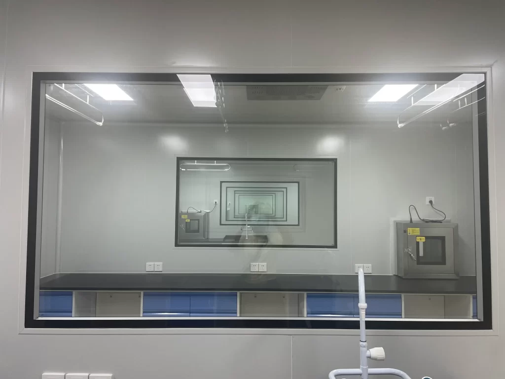 Cleanroom laboratory workspace with equipment visible through a large window, indicating a sterile working area.