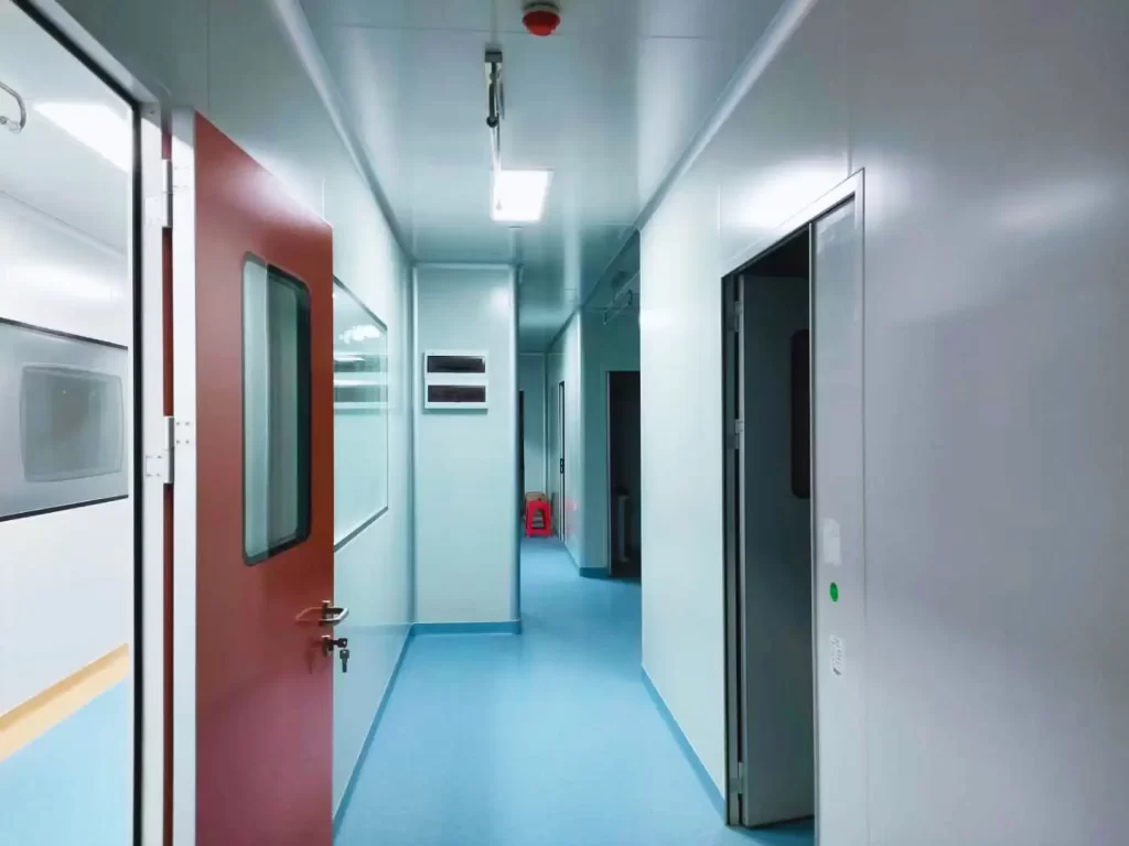 A cleanroom corridor with doors, one red door partially open and another door visible further down the hallway, under bright lighting.