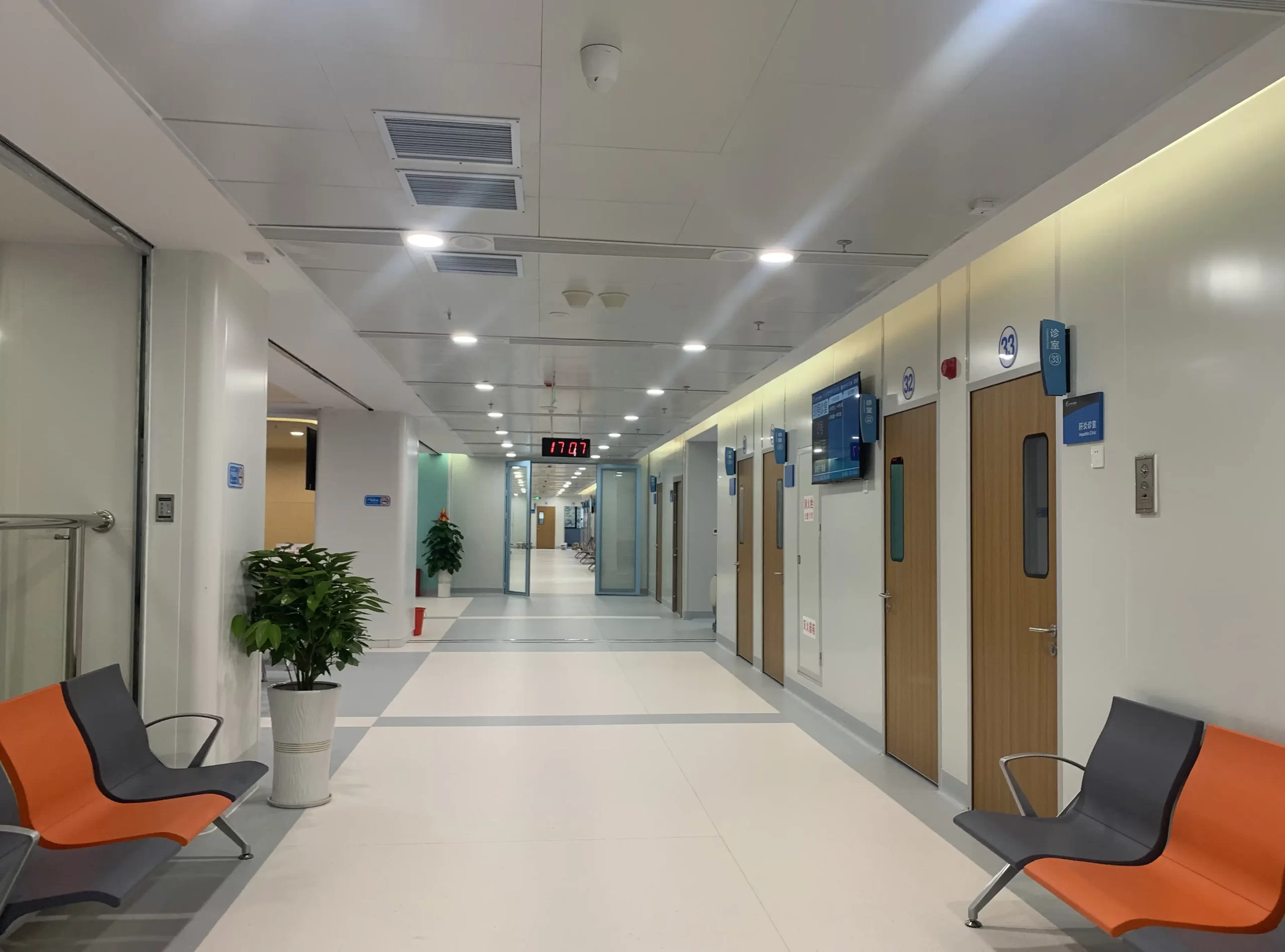 Real - scene of a hospital corridor with patient room doors on both sides, orange - gray seats, indicator signs at the end, and a clean and bright environment