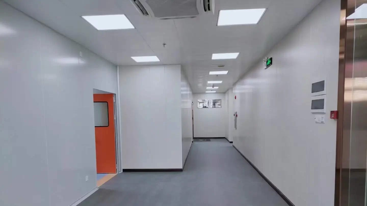 A long, brightly lit cleanroom corridor with white walls, a grey floor, and an orange door partially open on the left side.