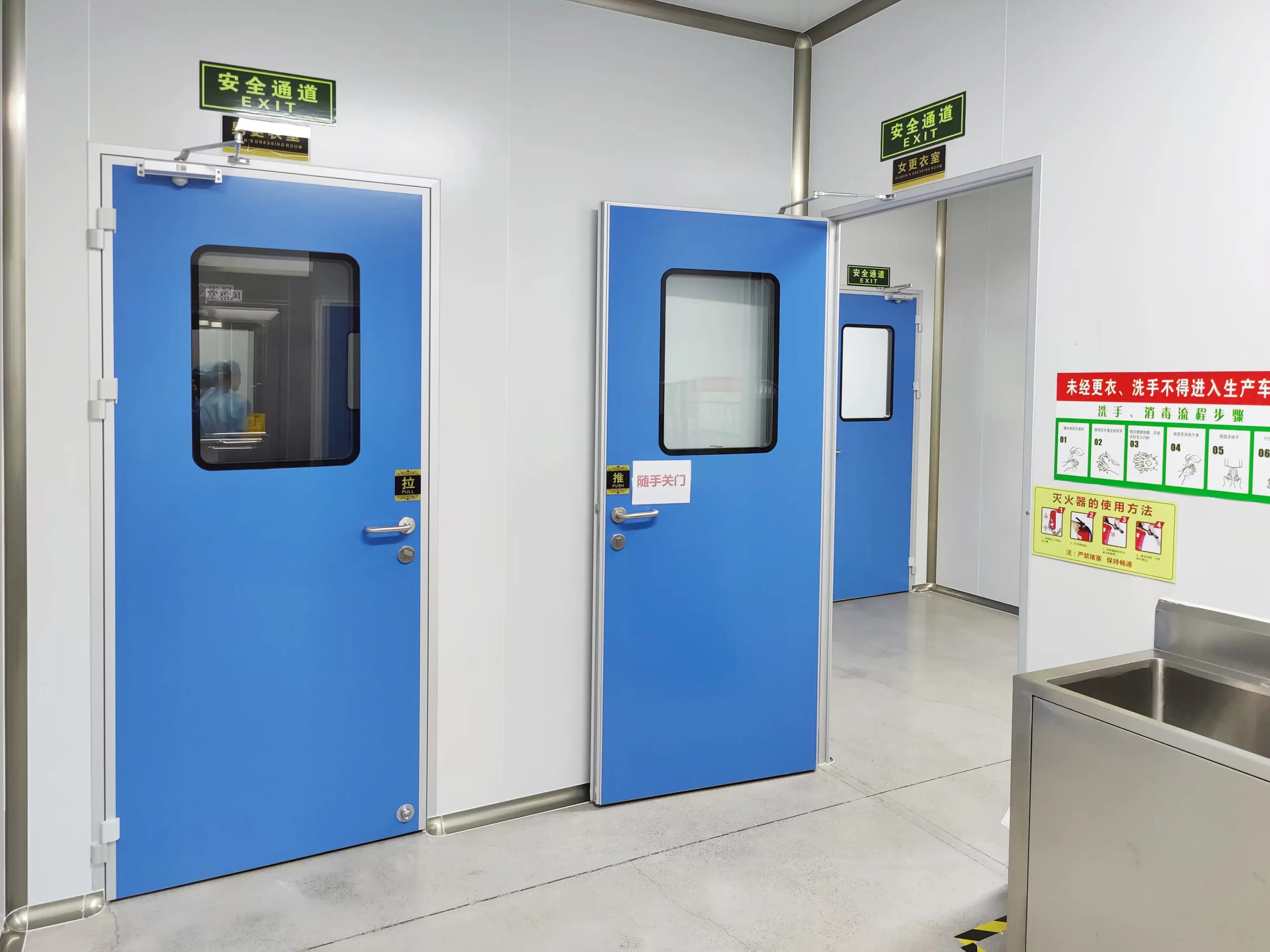 Multiple blue steel doors in a cleanroom, with safety channel signs. There is a stainless steel sink and operation specification signs nearby, presenting the compliant layout of cleanroom steel doors.