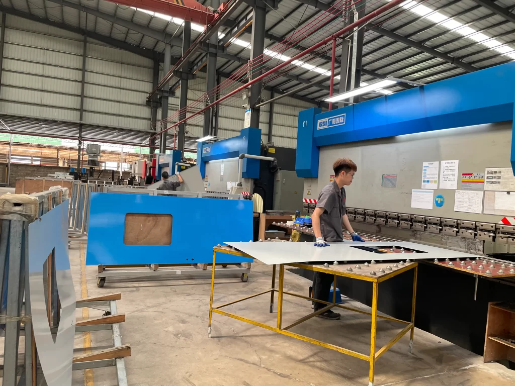 Factory worker processing cleanroom door panels with industrial machinery, demonstrating precision manufacturing for modular medical door production.