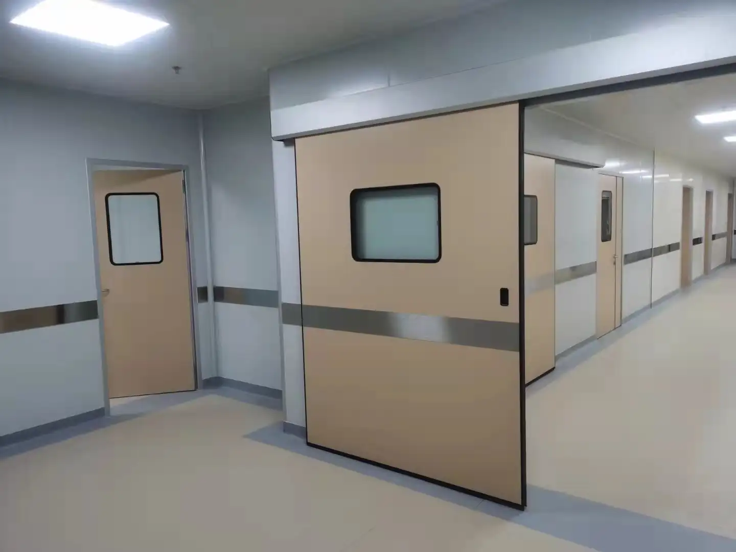 A sterile hospital corridor lined with modular cleanroom doors, including an automatic sliding unit, showcasing hygienic design and clinical environment integration.