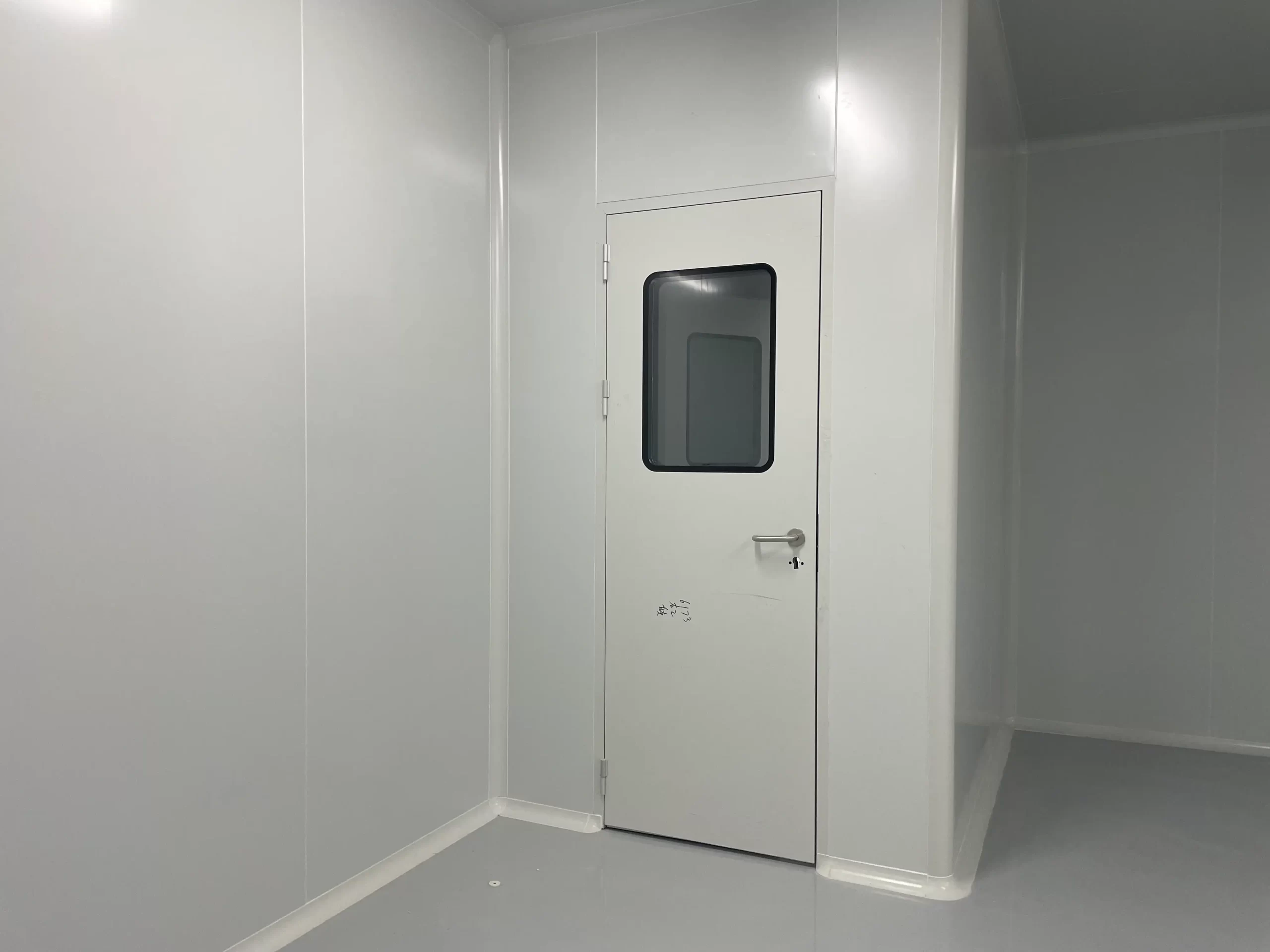A cleanroom accessory: white industrial cleanroom door with glass view window, in an empty food and beverage cleanroom with smooth wall panels.