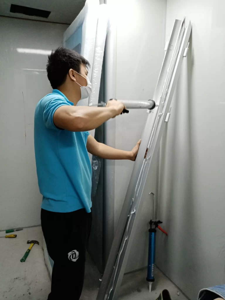 A worker applying cleanroom-grade sealant to a door panel as part of the cleanroom door installation process.