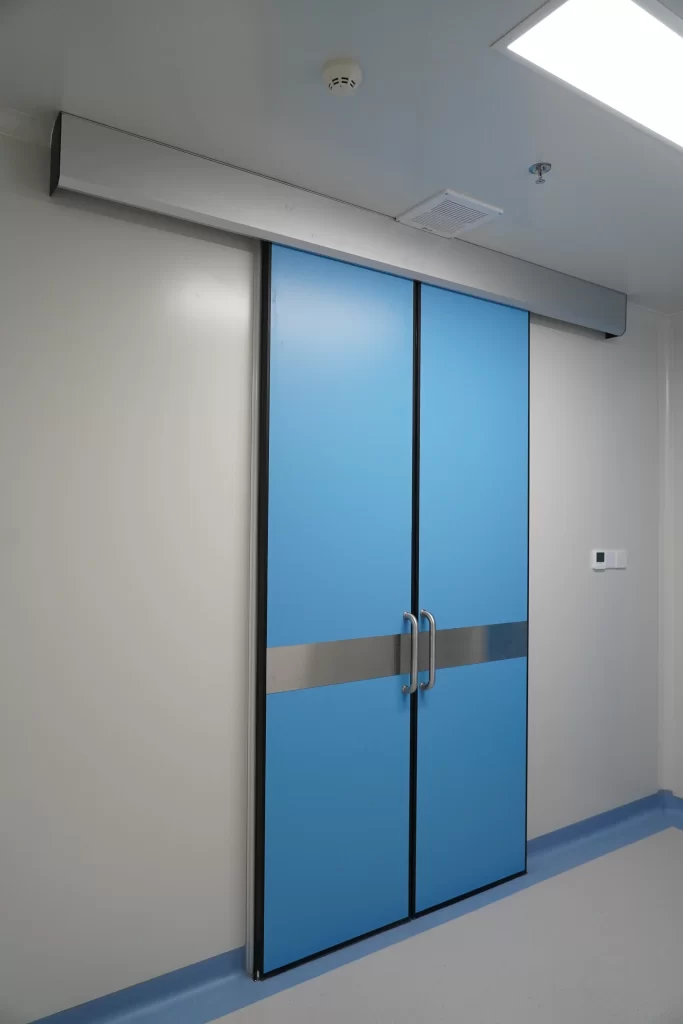 Blue double sliding door in a pharmaceutical cleanroom, with overhead track, stainless steel handles, and smooth, dust-free surfaces.