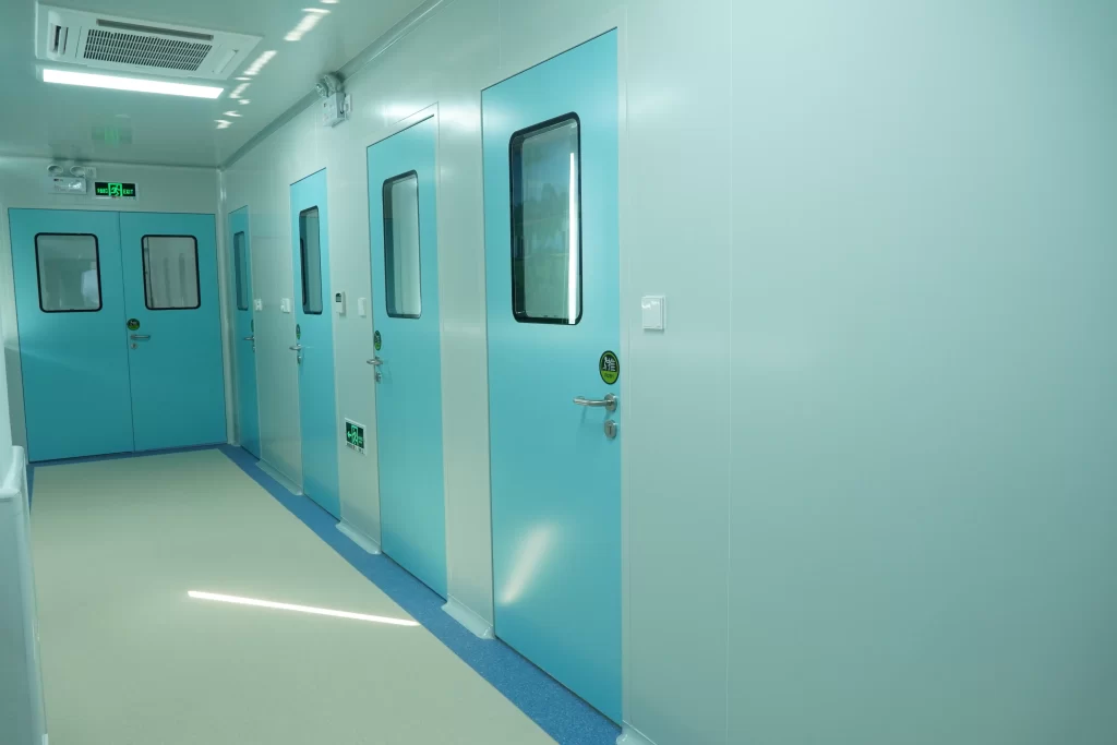 Row of light blue hermetic doors with observation windows in a pharmaceutical cleanroom corridor, showcasing airtight and contamination-controlled design.