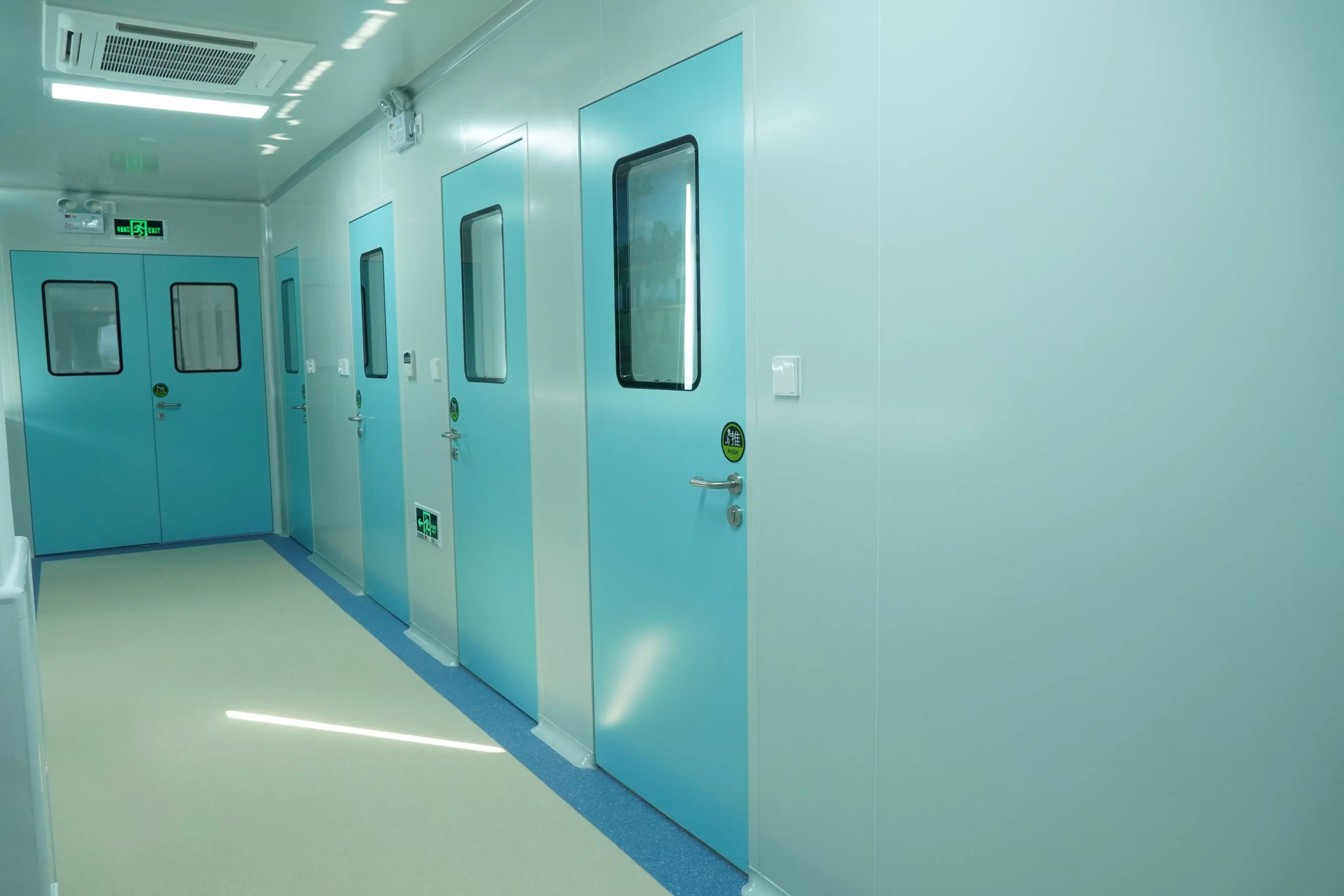 Row of light blue hermetic doors with observation windows in a pharmaceutical cleanroom corridor, showcasing airtight and contamination-controlled design.