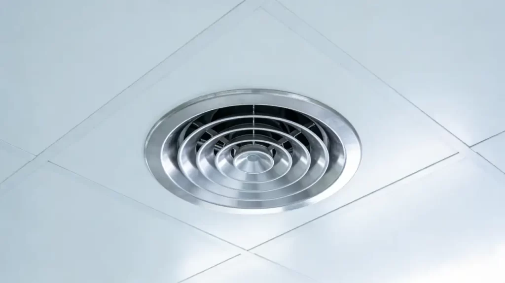 A stainless steel round diffuser (swirl type) installed flush in a cleanroom's white modular ceiling, with concentric circular blades for uniform airflow control.