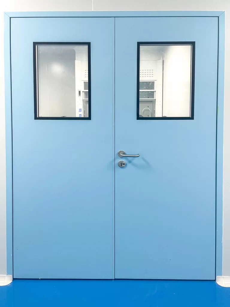 Close-up of a light blue double laboratory door with two vision panels, stainless steel handle, and cleanroom finish.