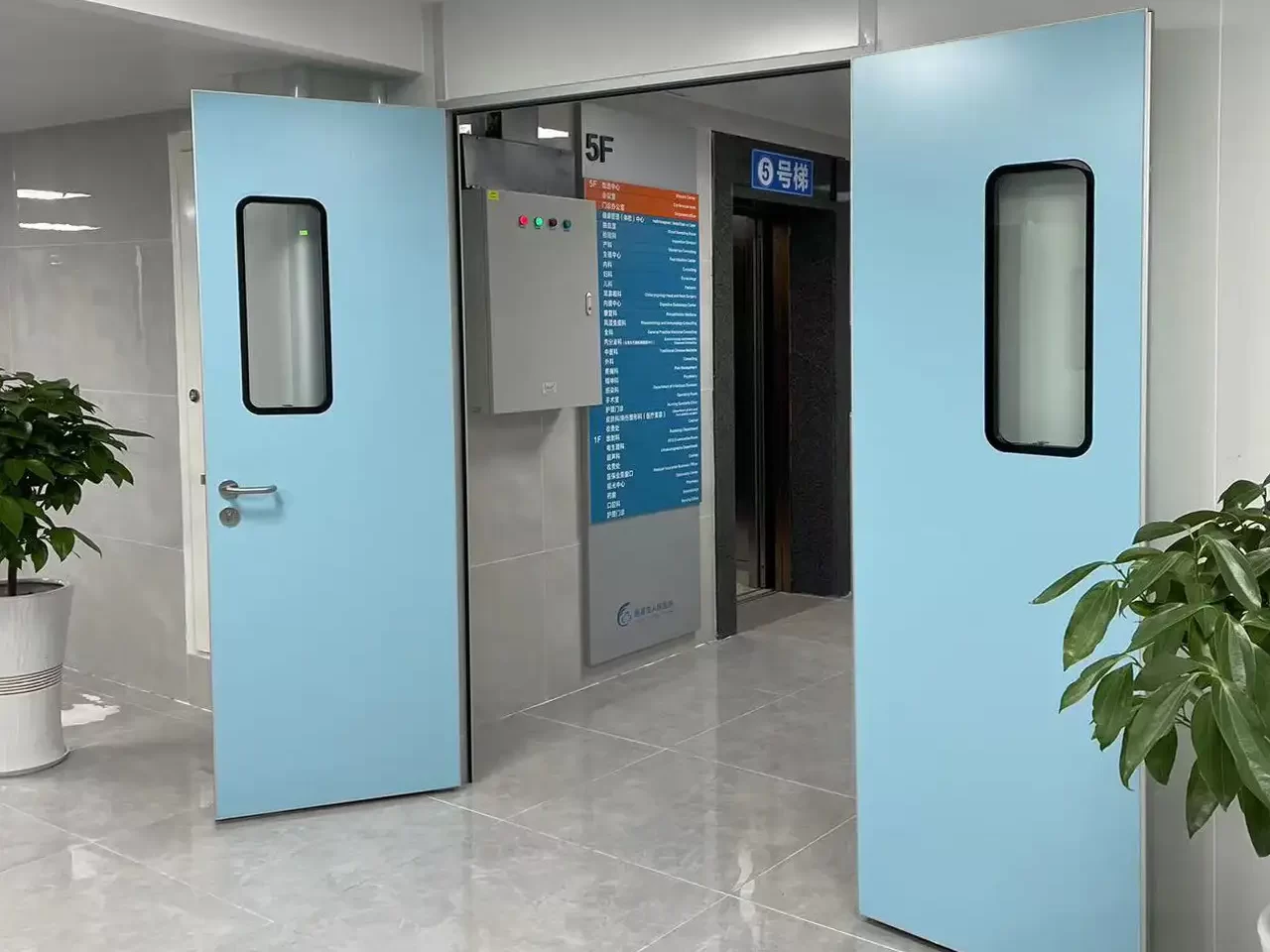 Open light blue hospital double doors revealing a polished tile corridor, elevator lobby, and floor directory sign.