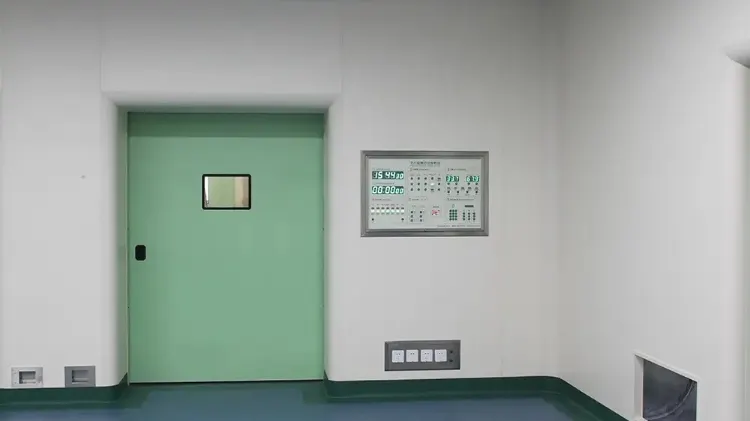 Green airtight cleanroom door with a small window next to a digital control panel in a sterile facility.