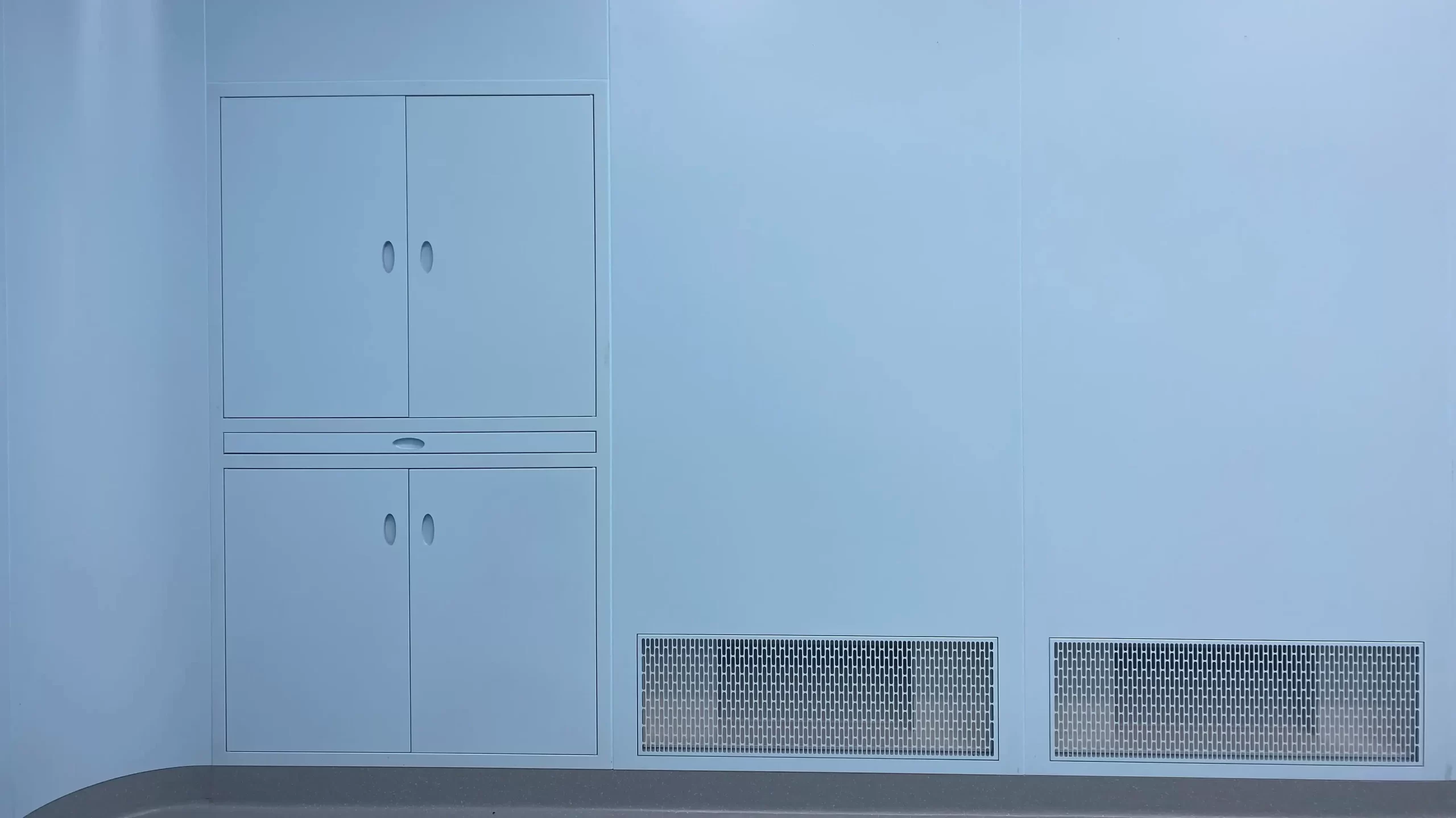 Cleanroom wall section next to the door, showing built-in airtight storage cabinets and low-level return air grilles.