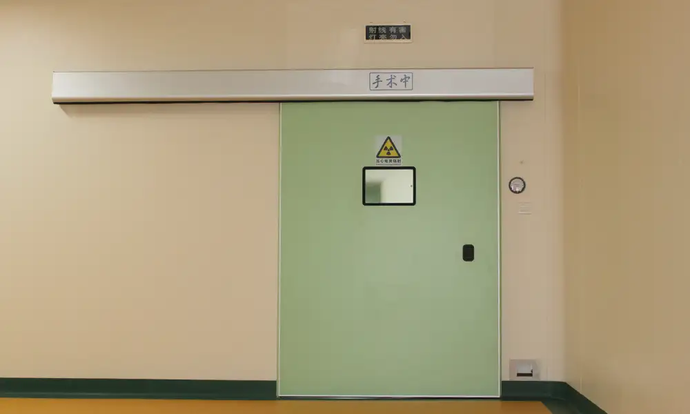 Automatic hermetic sliding operating room door featuring a radiation warning sign and overhead status display.