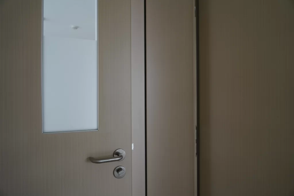 Close-up view of HPL cleanroom door surface, frosted observation window, stainless lever handle and lock, showing HPL panel edge banding detail.