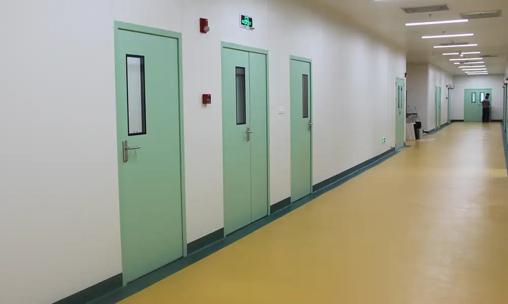 Light green hygienic doors with vertical windows lining a sterile hospital corridor with seamless yellow flooring.
