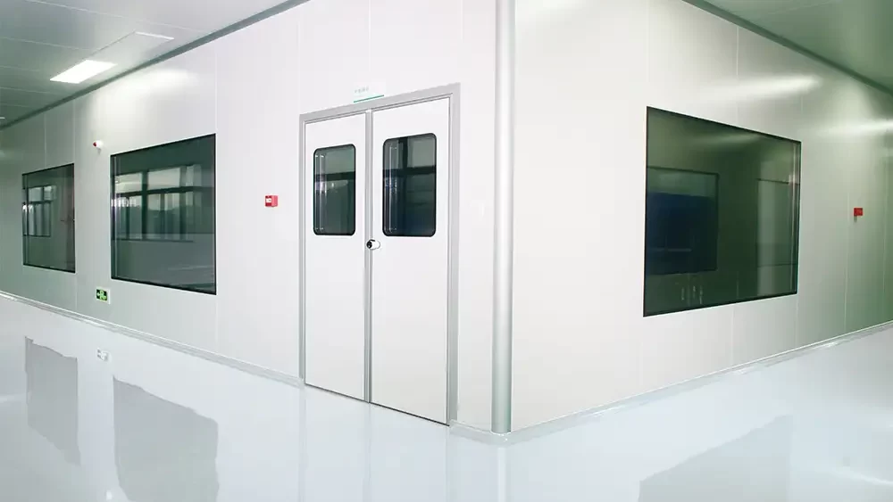 A bright pharmaceutical cleanroom corridor featuring white double doors with vision panels and large wall windows.