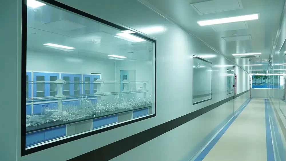 Bright pharmaceutical cleanroom corridor with a large glass window overlooking a production area with blue cabinets.