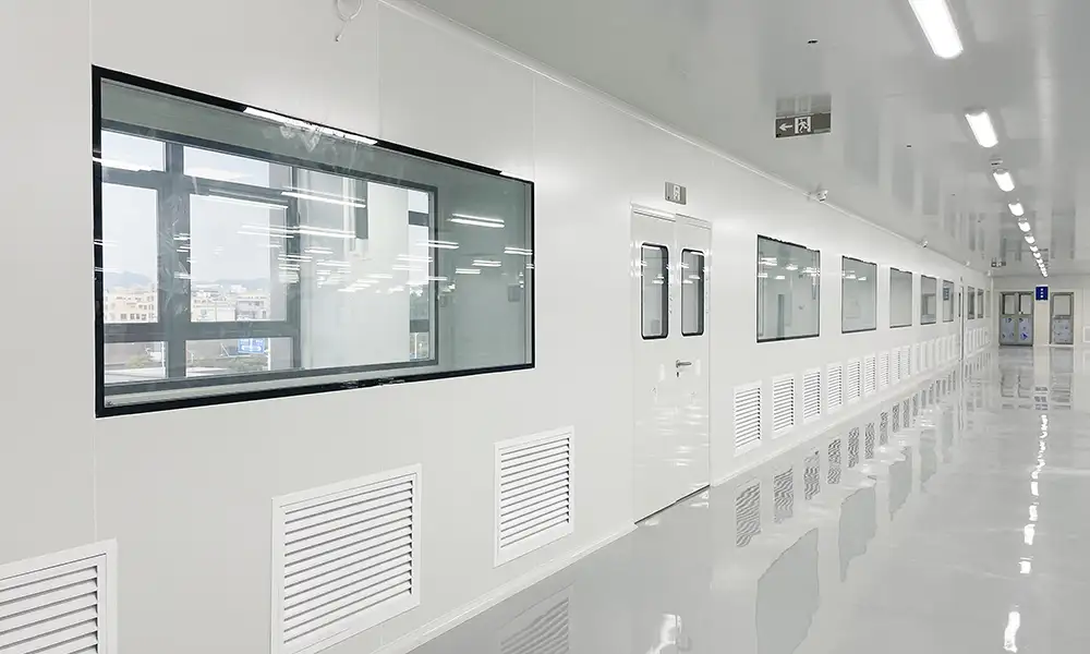 A bright corridor featuring a white pharmaceutical cleanroom door with large observation windows and reflective floors.