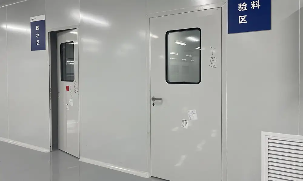 White pharmaceutical cleanroom door with rectangular viewing panels and blue signs for glue and material inspection.