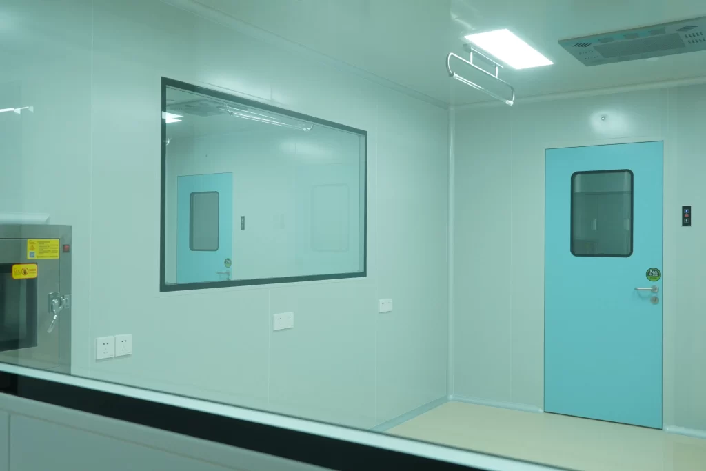 Food Processing Doors: Light blue sanitary swing door with observation window in food manufacturing cleanroom, smooth non-porous wall panels, sterile high-care hygiene production zone interior.