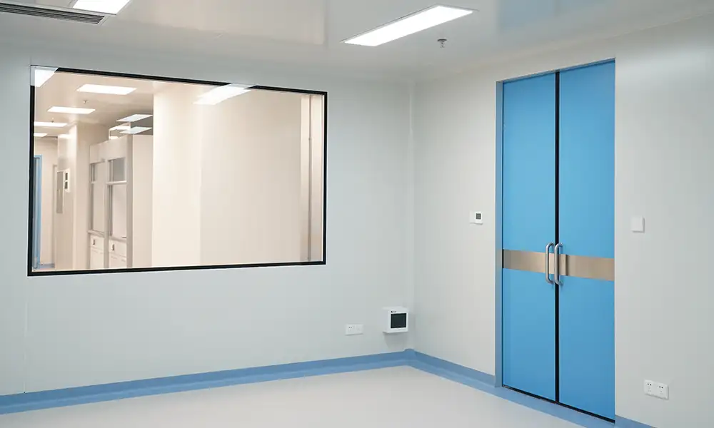 Blue double swing laminate cleanroom door with metal crash bar, adjacent cleanroom observation window, empty GMP-grade controlled cleanroom interior.