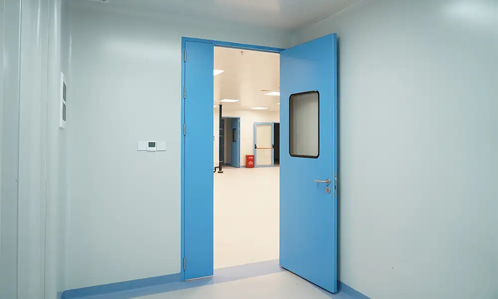 Open blue single swing laminate cleanroom door with vision window, flush cleanroom wall panels, controlled pharmaceutical GMP environment for contamination control.