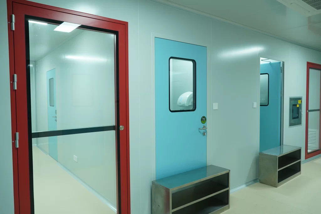 Cleanroom corridor featuring a red-framed glass fire exit door, a blue single door, and stainless steel benches.