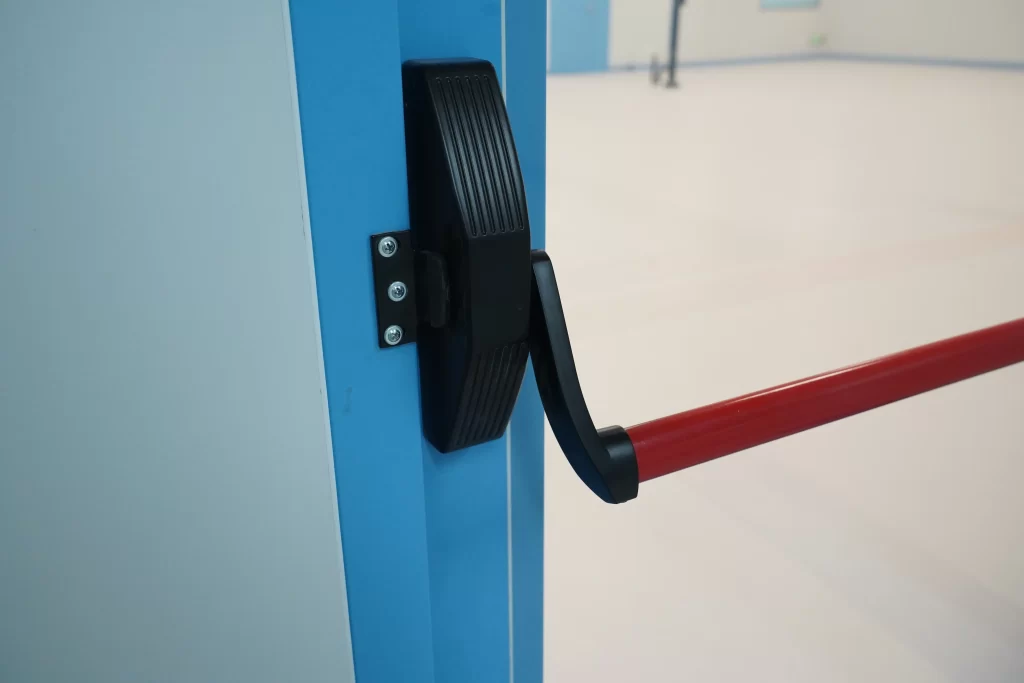 Close-up of sanitary hardware for Panic Push Bar Doors, embedded mounting on blue cleanroom door frame eliminating contamination dead zones.