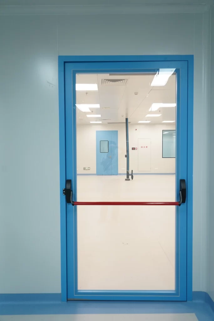 Blue frame cleanroom single glass Panic Push Bar Doors, red emergency panic bar installed inside pharmaceutical cleanroom with modular wall panels.