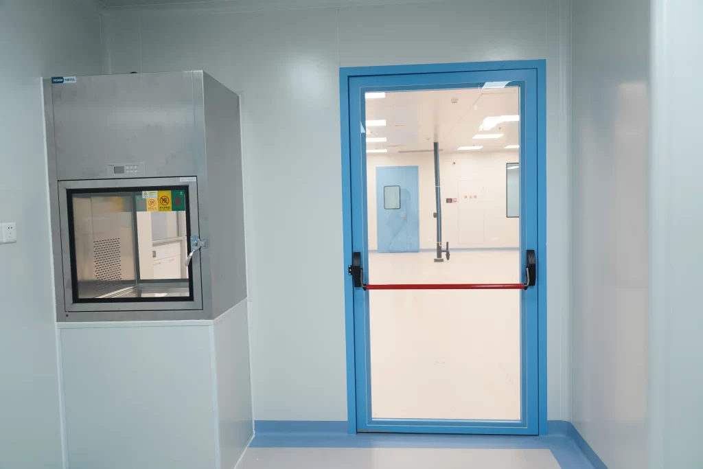 Sterile workshop view of Panic Push Bar Doors, cleanroom emergency exit door next to stainless steel transfer pass box in pharmaceutical facility.