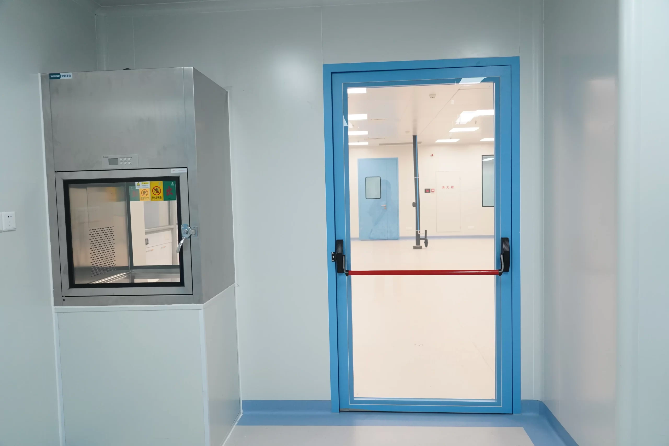 Sterile workshop view of Panic Push Bar Doors, cleanroom emergency exit door next to stainless steel transfer pass box in pharmaceutical facility.