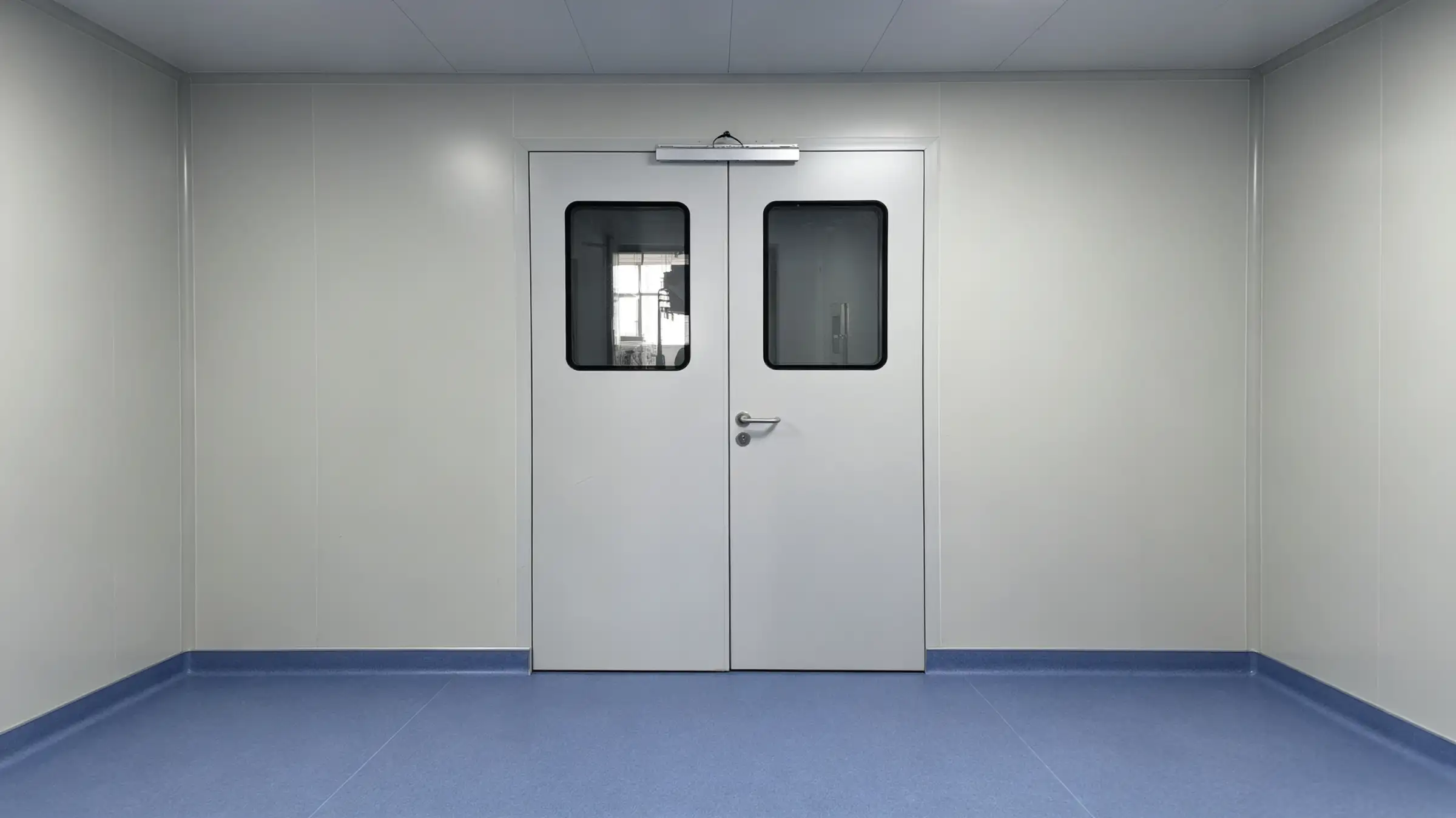 White stainless steel double doors with viewing windows and a closer mechanism in a room with white walls and blue flooring.