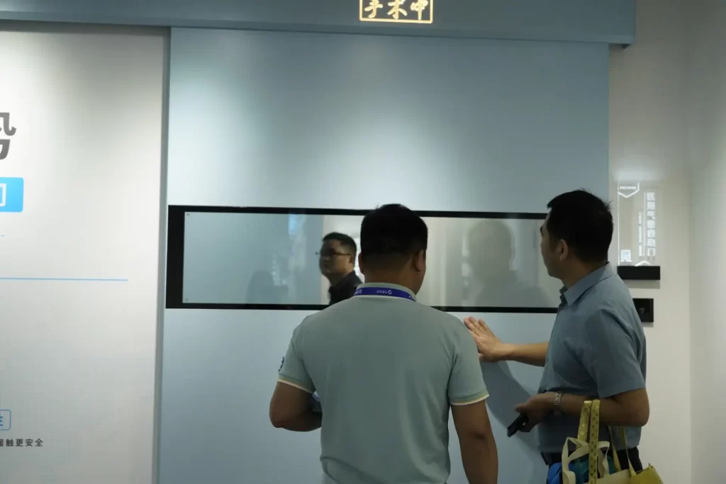 Visitors inspecting an E-ZONG light blue automatic hermetic sliding door with a narrow vision window panel designed for hospital operating rooms and cleanroom environments.