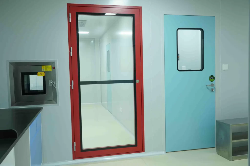 E-ZONG pharmaceutical cleanroom setup showing a red-framed airtight glass door alongside a light blue swing door and stainless steel pass box.