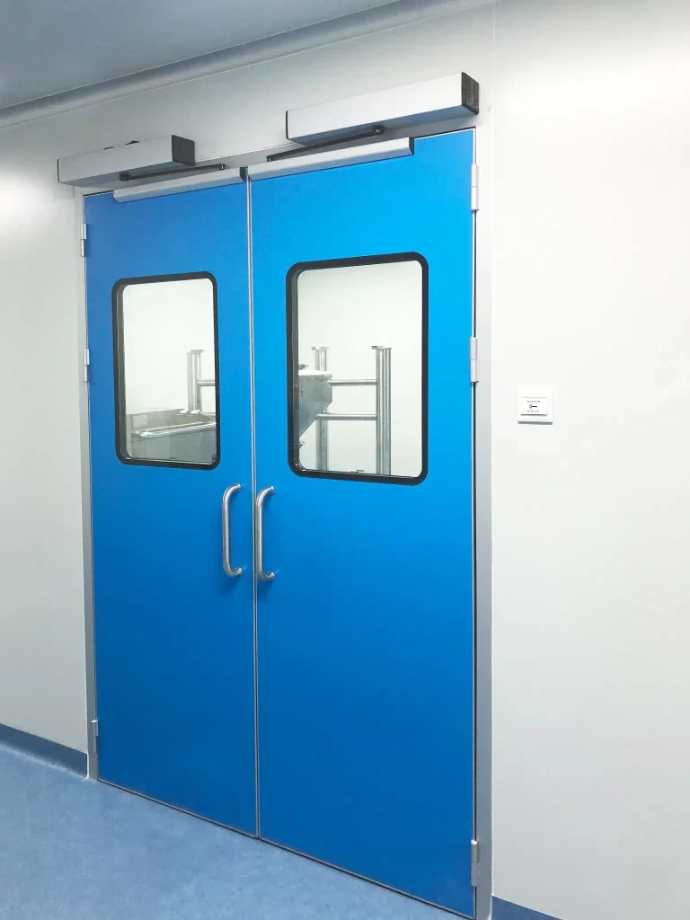 E-ZONG blue double-leaf automatic swing cleanroom door featuring large observation windows, stainless steel push handles, and top-mounted automatic door operators installed in a pharmaceutical production facility