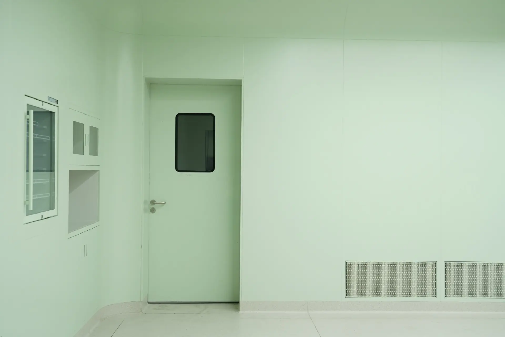 E-ZONG single swing cleanroom door featuring a glass vision panel, flush-mounted wall system, pass-through box, and integrated return air grill in a green-tinted pharmaceutical cleanroom environment.