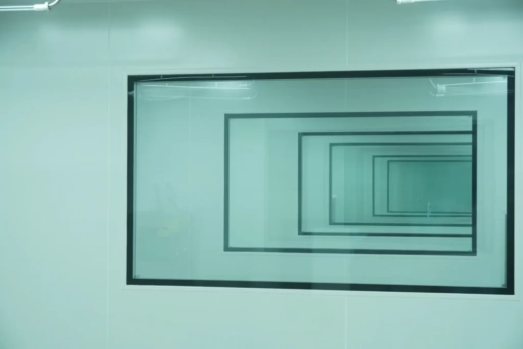 Flush-mounted double-glazed cleanroom viewing window (vision panel) providing multi-room line-of-sight monitoring without breaking the air seal