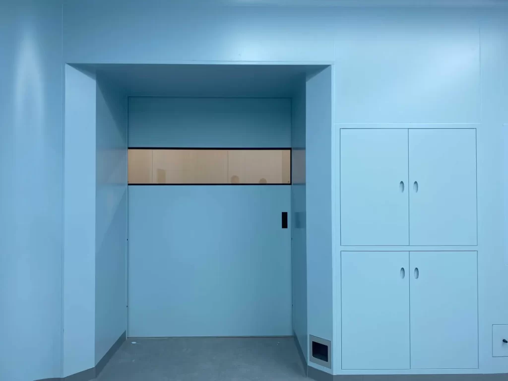 E-ZONG light blue hermetic sliding door with a narrow double-glazed vision panel installed flush in a medical facility cleanroom.