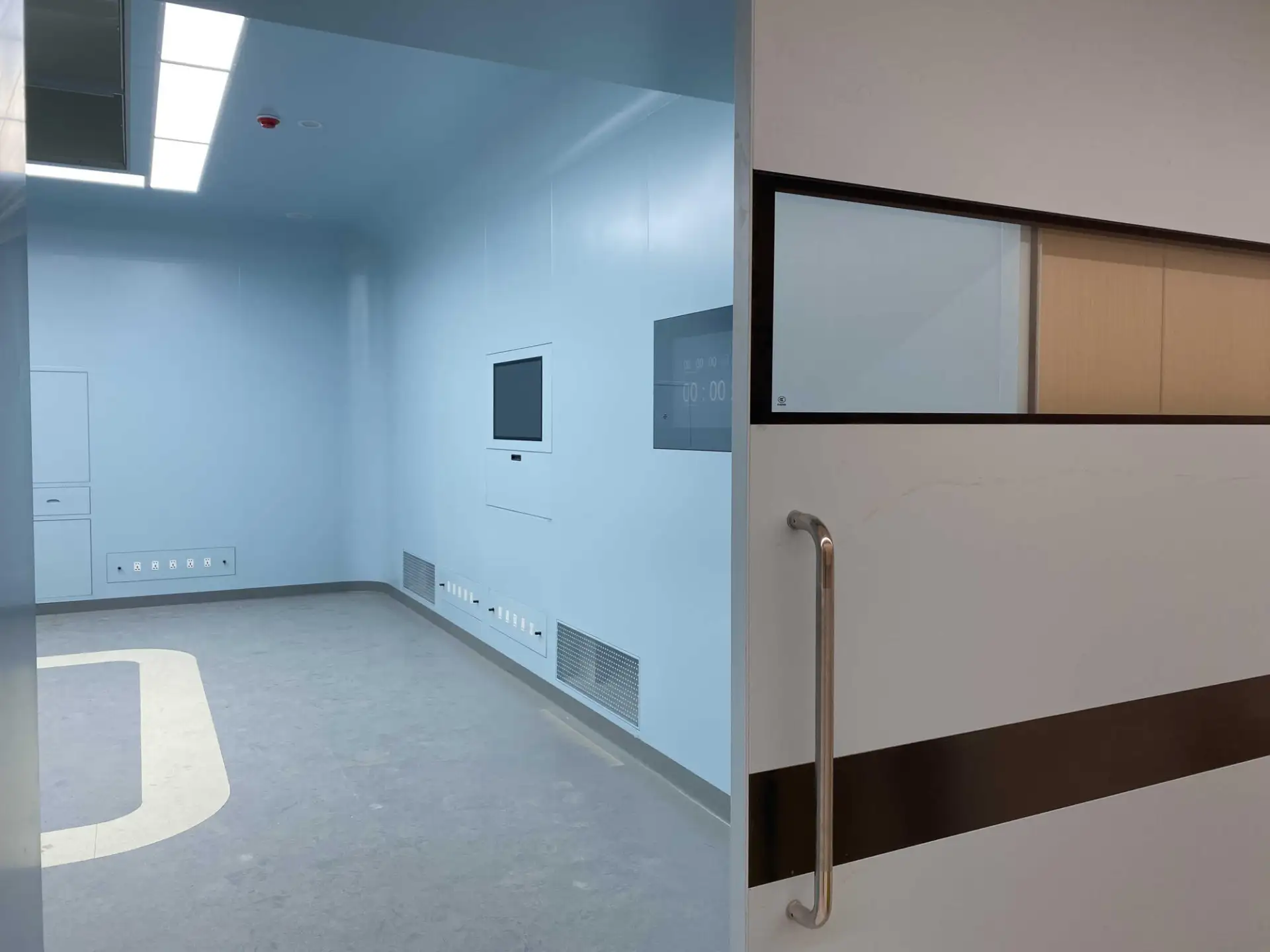 Open E-ZONG airtight sliding door with stainless steel handle, revealing a sterile hospital operating room suite with wall-mounted control panels