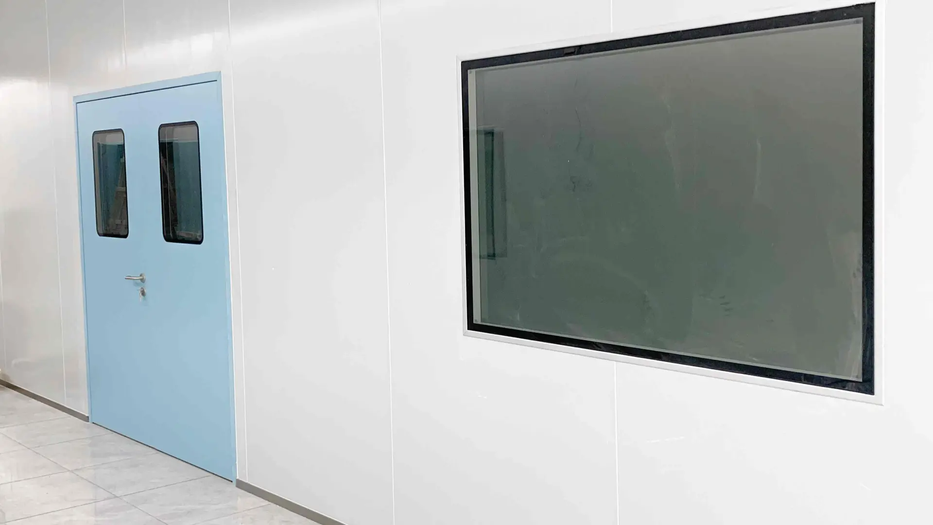 Closed light blue single swing laminate cleanroom door with dual vision windows, flush cleanroom wall panels, large observation window, controlled environment corridor