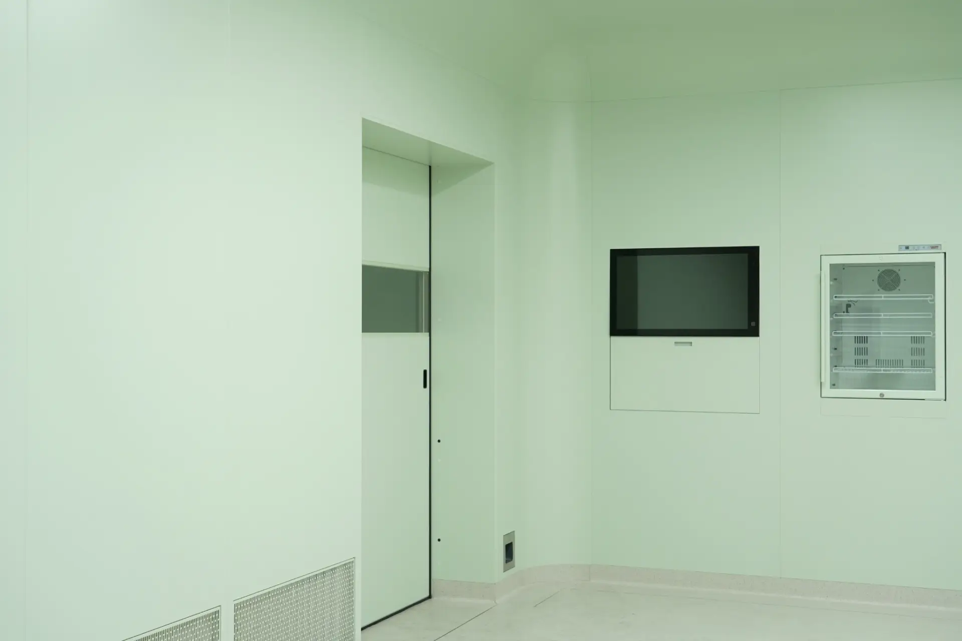 Closed light green single swing laminate cleanroom door with horizontal vision window, flush cleanroom wall panels, wall-mounted monitor and glass-fronted cabinet, controlled environment