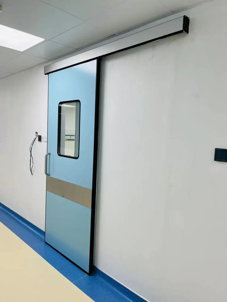 E-ZONG light blue automatic hermetic sliding door with a vertical observation window and stainless steel kick plate installed along a medical cleanroom corridor.
