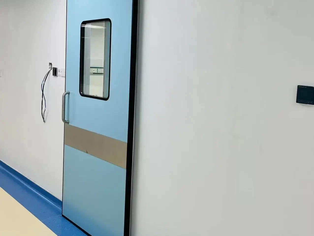 E-ZONG light blue automatic hermetic sliding door with a vertical observation window and stainless steel kick plate installed along a medical cleanroom corridor.